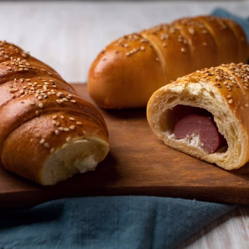 Sabanita | Pastelería Ciro Guatemala | Delicada y deliciosa, nuestra sabanita salada está elaborada con una suave masa horneada a la perfección rellena con salchicha de pavo y un cremoso toque de queso crema que se funde en cada bocado. Decorada con ajonjolí para un acabado crujiente y aromatico, es el equilibrio ideal entre sabor y textura.